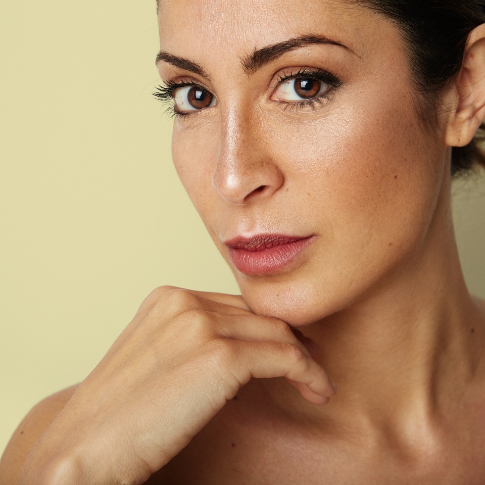 Beautiful young woman with clean skin, natural make-up over empty yellow color background. Close up portrait. Fashion and healthcare cosmetic facial skin concept. Copy paste text space