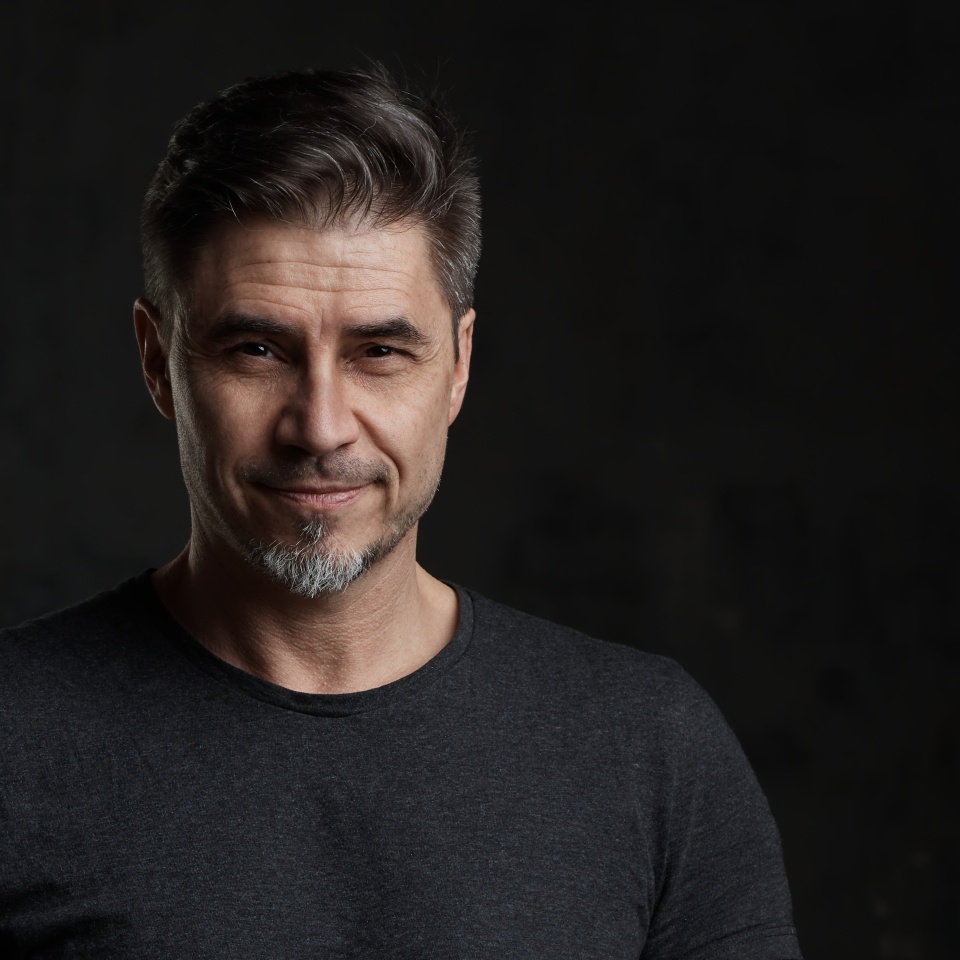 Portrait of happy older man in casual tshirt smiling isolated on dark background.