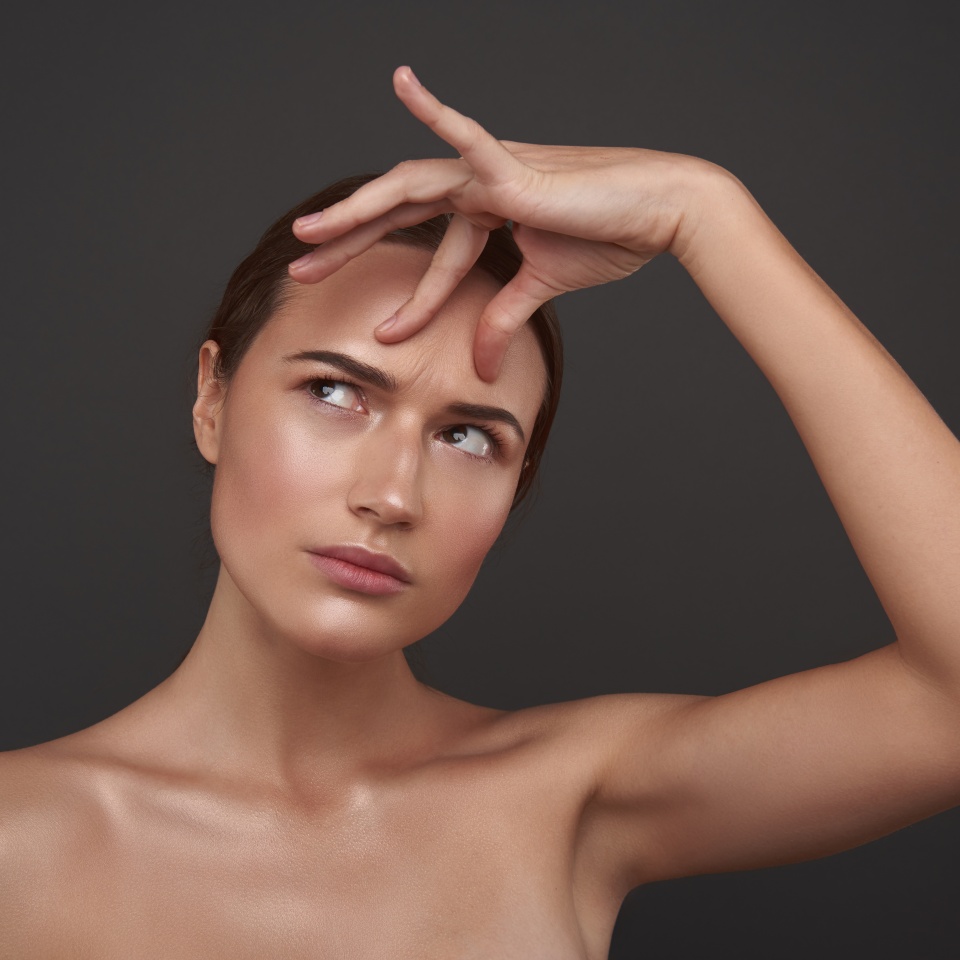 Close up portrait of displeased lady with naked shoulders checking the existence of frown lines. Isolated on gray background