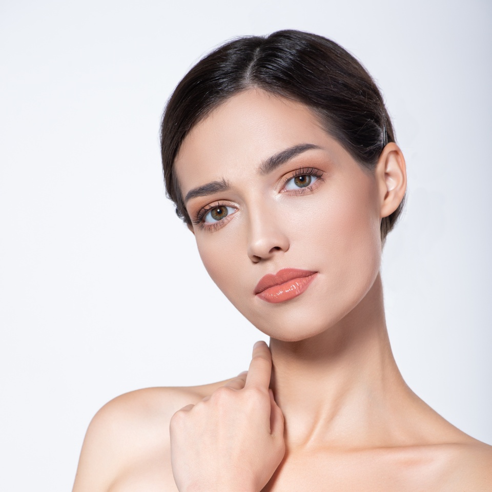 Portrait of beautiful brunette girl which touching her fresh face. Beautiful face of young woman with health fresh skin. Beautiful face of young adult woman with clean fresh skin. Skin care.