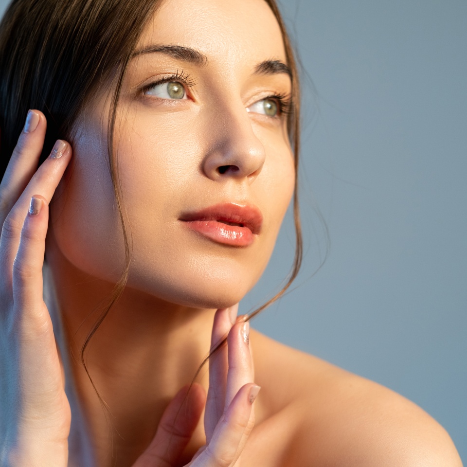 Skin rejuvenation. Aesthetic cosmetology. Facelift treatment. Woman with nude makeup touching flawless radiant face isolated on blue copy space background.