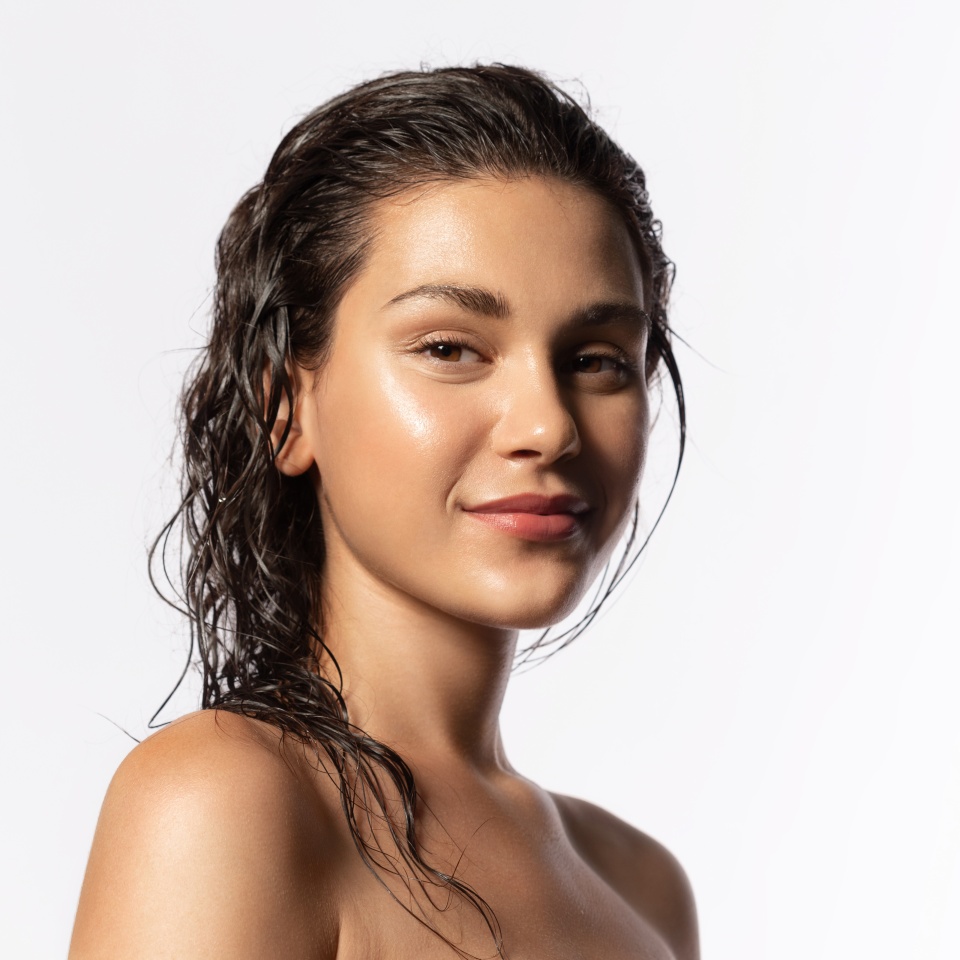 Beautiful young woman with clean perfect glowing skin, wet hairs. Portrait of smiling girl with bare shoulders on gray studio background. Skincare and wellness. Natural woman beauty.