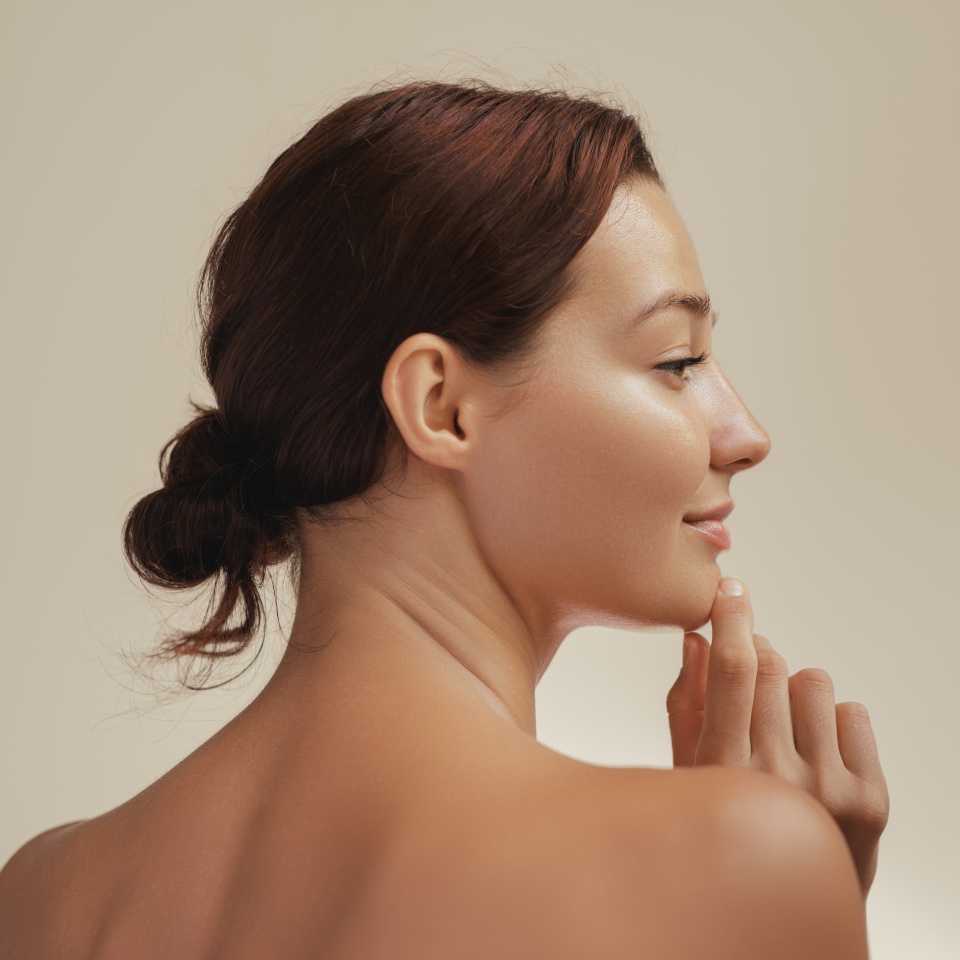 Side profile portrait of a young Caucasian woman with glowing, smooth skin, gently touching her chin. Ideal for skincare, beauty, and wellness concepts. High-quality image for cosmetic campaigns.