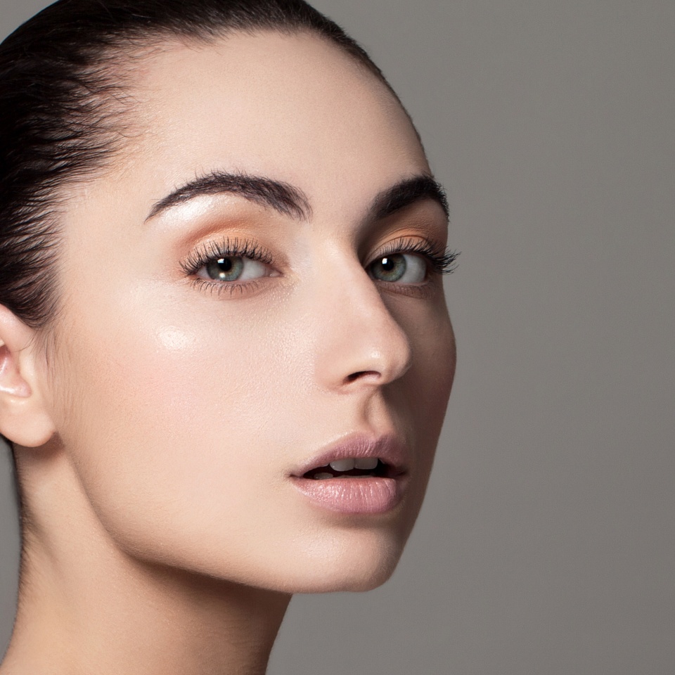 Beautiful face of young adult woman with clean fresh skin and bare shoulders on grey background.