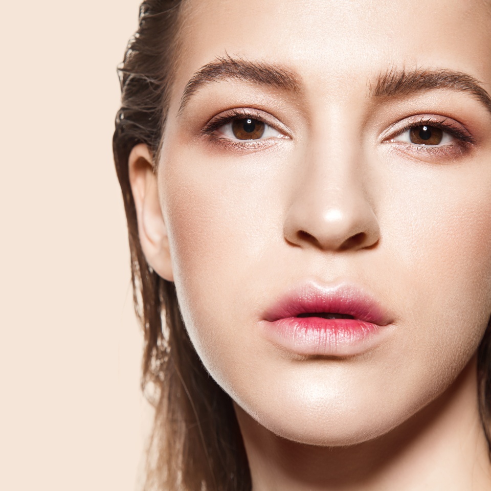Close-up face of fashionable girl with natural make-up and clean beautiful skin looking at camera on beige background