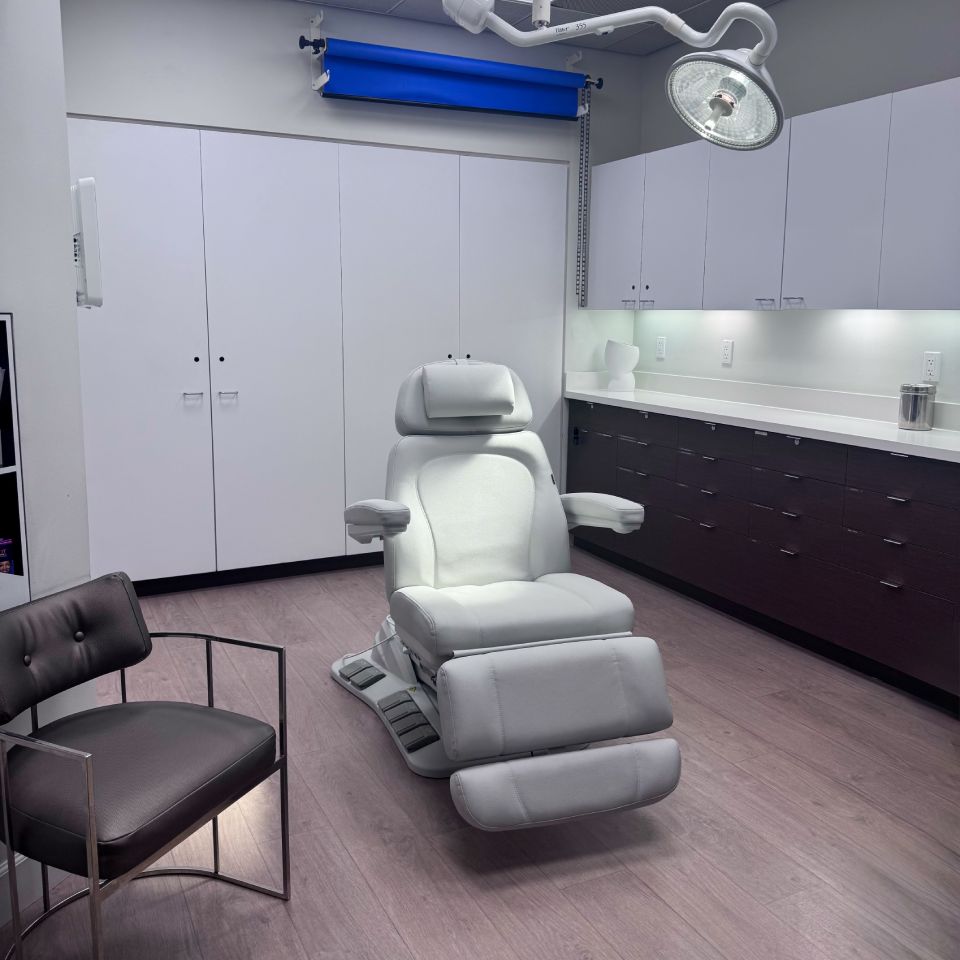 A modern medical room with a white reclining chair, stool, cabinets, countertop supplies.