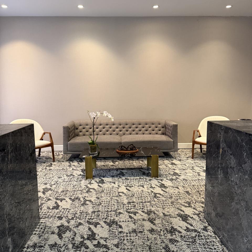 Elegant waiting area at Sayah Institute with a tufted gray sofa, marble coffee table, and modern seating on a patterned carpet