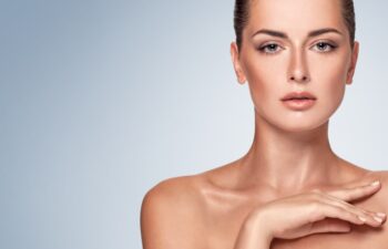 Beautiful face of young adult woman with clean fresh skin and bare shoulders. Beauty young girl with soft silky skin, hand touching his shoulder. Isolated on blue background