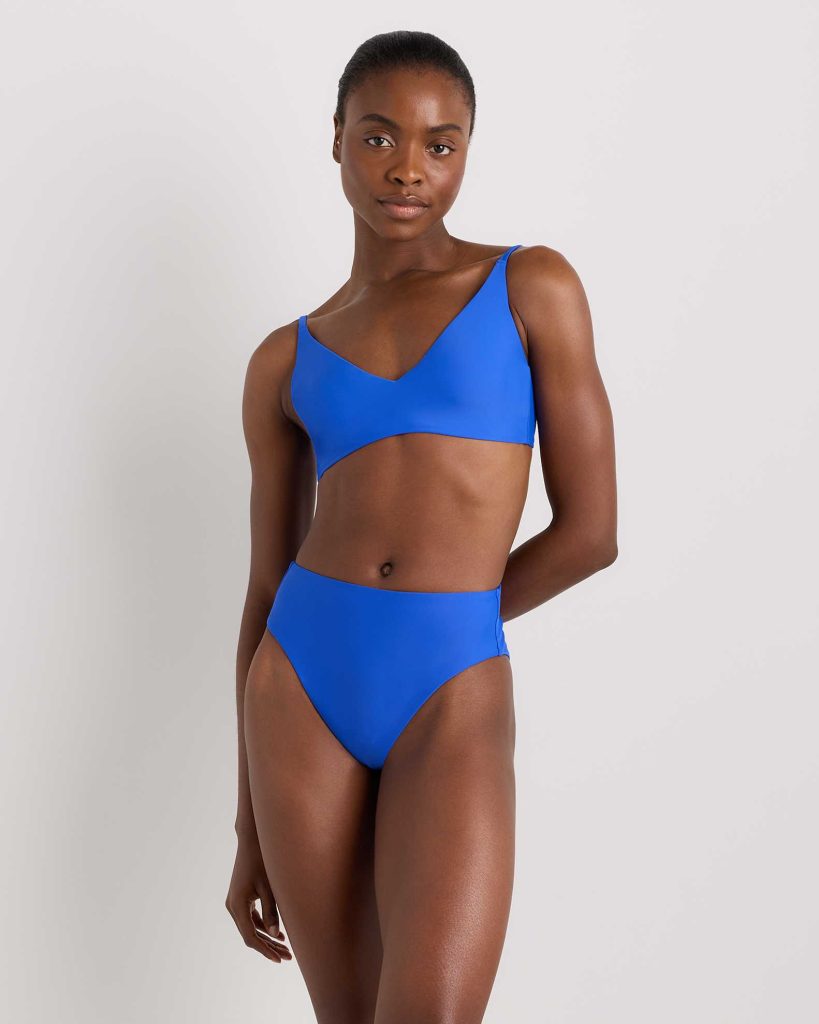 A person stands against a plain background wearing a bright blue bikini with a V-neck top and high-waisted bottoms.